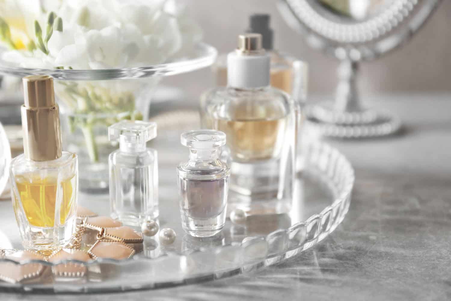 Glass tray with perfume bottles on grey table